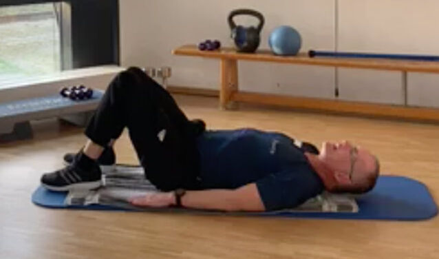Fitnesstrainer macht Übung vor: Er liegt mit angewinkelten Beinen auf dem Rücken.