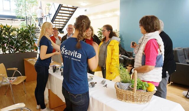 Zwei Ernährungsberaterinnen der savita stehen an ihrem Stand. Davor sind eine Reihe Besucherinnen zu sehen, die an den Duftproben schnuppern.